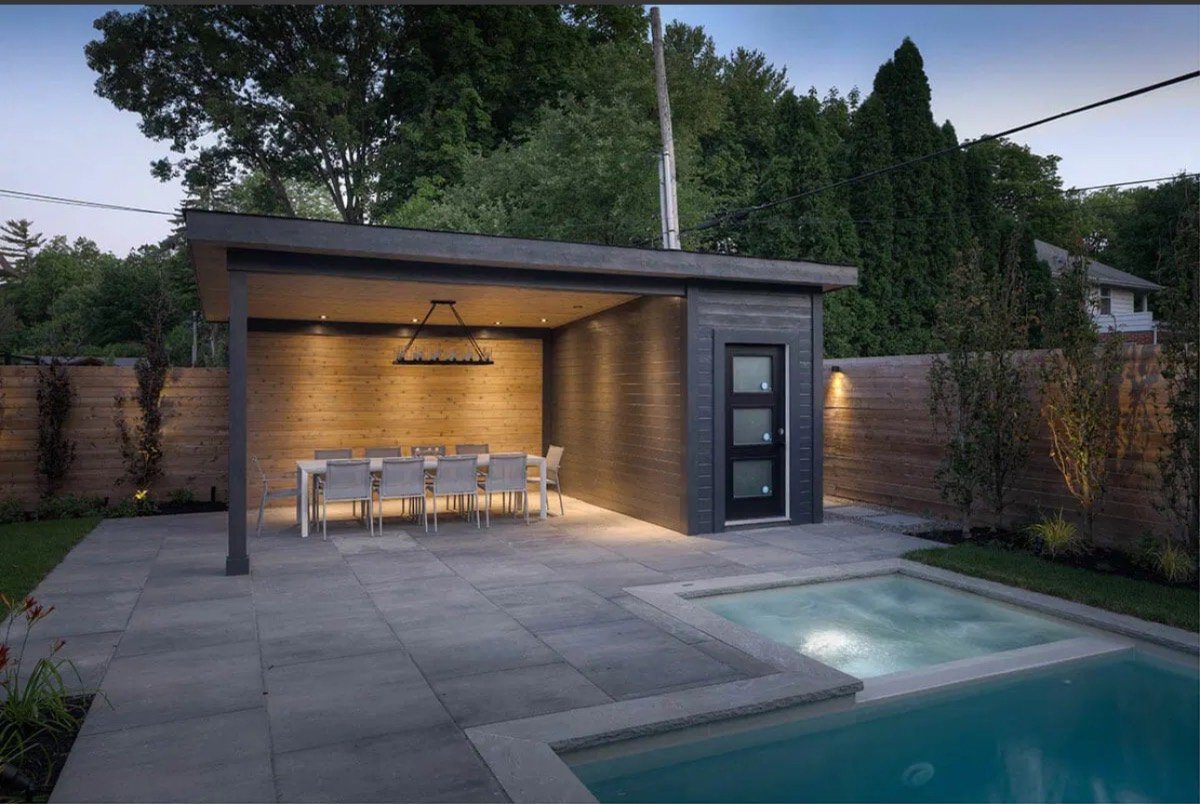 A lit wood cabana dining pavilion beside a plunge pool at twilight in an Ottawa backyard