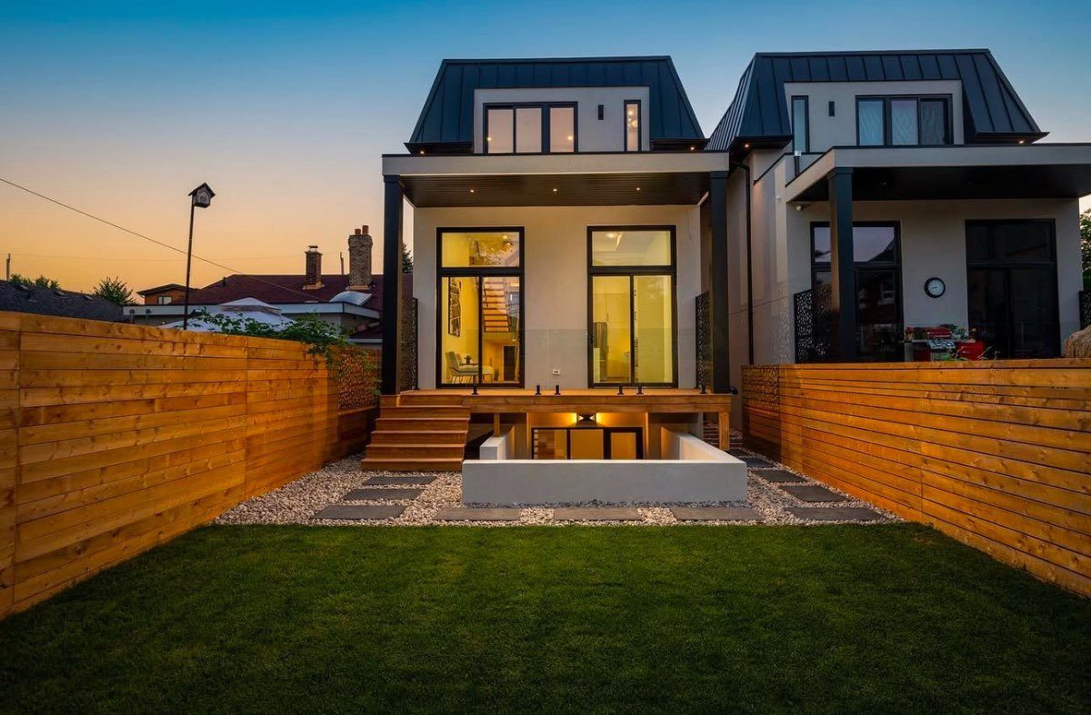 A lit modern Ottawa home at twilight framed by horizontal cedar privacy fencing and a fresh lawn