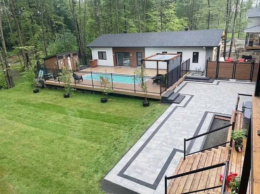 Elevated overview of a backyard with an interlock patio, pool and black fencing